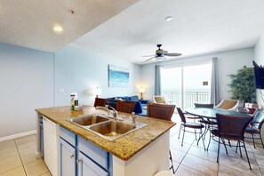 A modern kitchen with granite countertops, stainless steel appliances, and a dining area with a round table and chairs. - Tropical-themed condo with bi-level pool, fitness center & beach access (Panama City Beach)