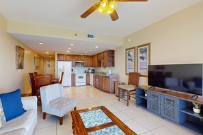 A spacious living area with a dining table, chairs, a sofa, a TV, and a kitchen in the background. - Beachfront Condo, gorgeous views, shared pool and beach access (Panama City Beach)