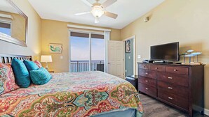 Ein Schlafzimmer mit einem großen Bett, einem Schminktisch, einem Fernseher und einem Deckenventilator.