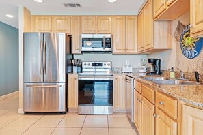 A modern kitchen with stainless steel appliances, wooden cabinets, and a granite countertop. - Gulf front condo with resort amenities, snack bar, and Lazy River (Panama City Beach)