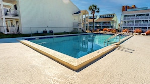 A swimming pool with a white building and a palm tree in the background. - Condo in Panama City Beach with pool & beach access (Panama City Beach)