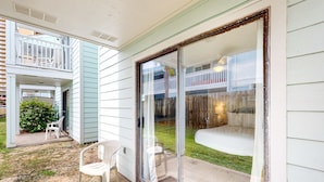 A residential patio with a sliding glass door, a small outdoor seating area with two chairs, and a visible backyard with a wooden fence and a pool. - Condo in Panama City Beach with pool & beach access (Panama City Beach)