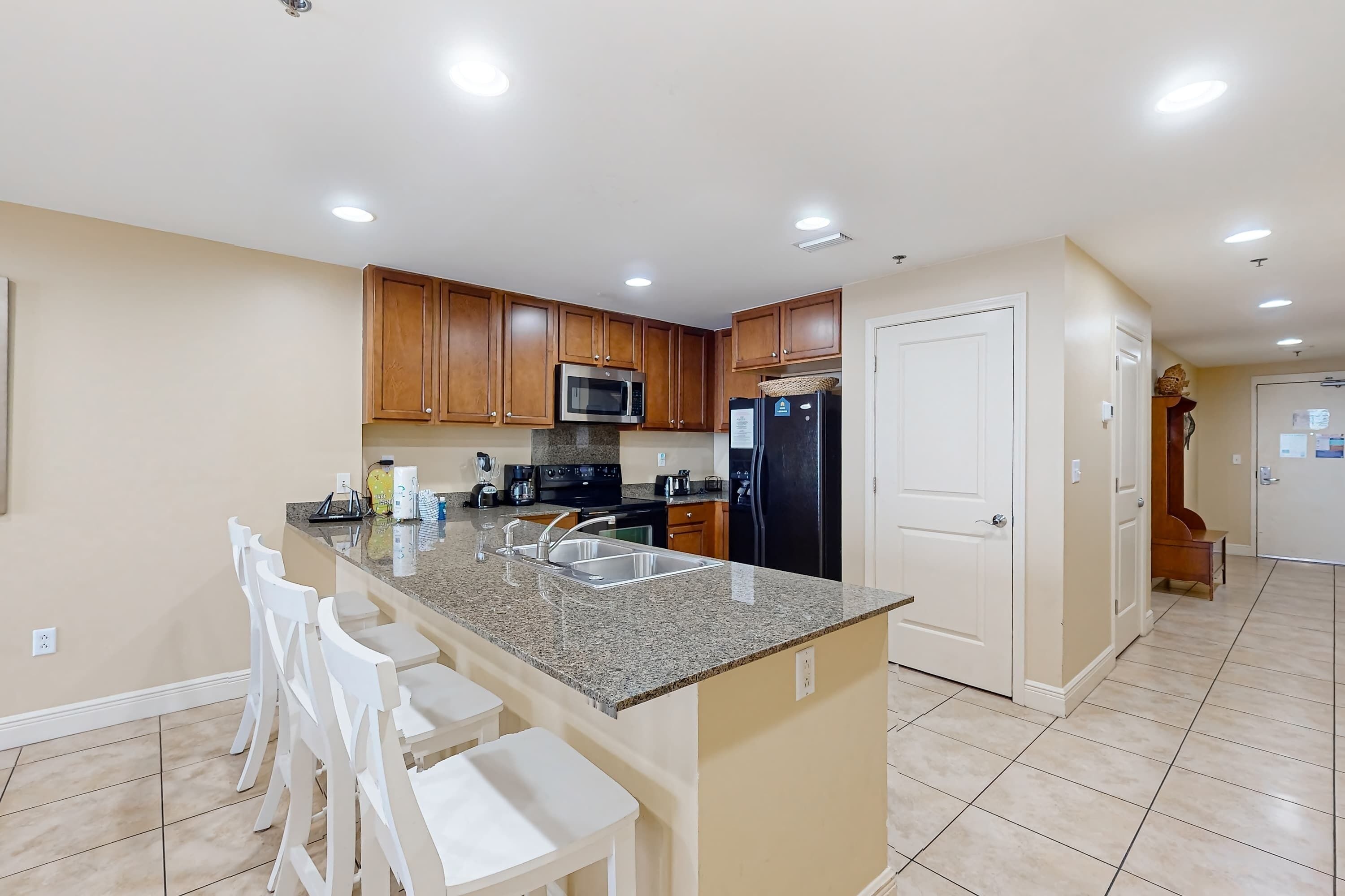 A modern kitchen with granite countertops, wooden cabinets, a built-in microwave, a refrigerator, and a sink.
