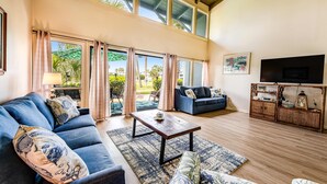 A spacious living area with a high ceiling, a large TV, and a comfortable seating arrangement. - Convenient condo with WiFi, W/D, shared pool, tennis, & bocce, and more (Panama City Beach)