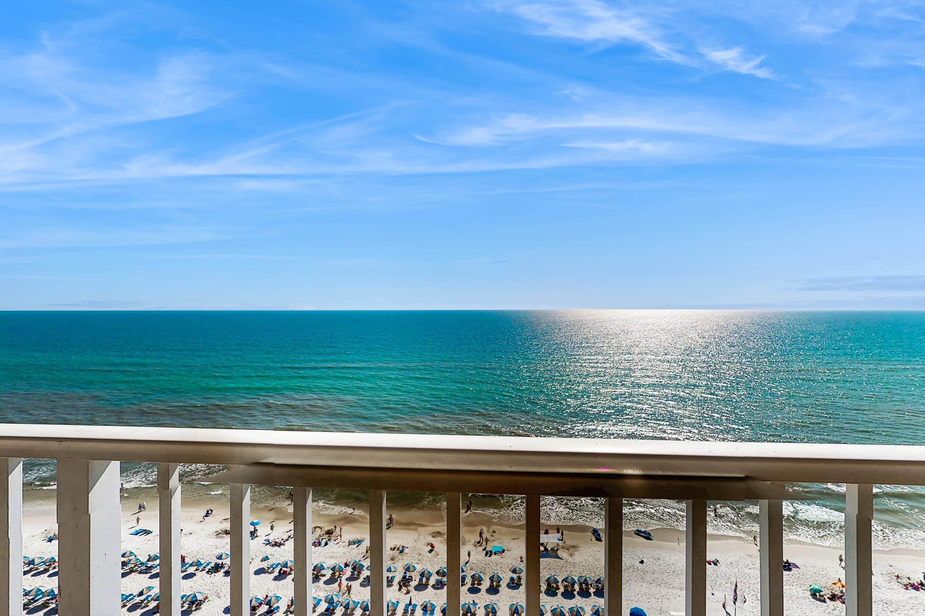 A beach with numerous umbrellas and people, a clear sky, and a view of the ocean.