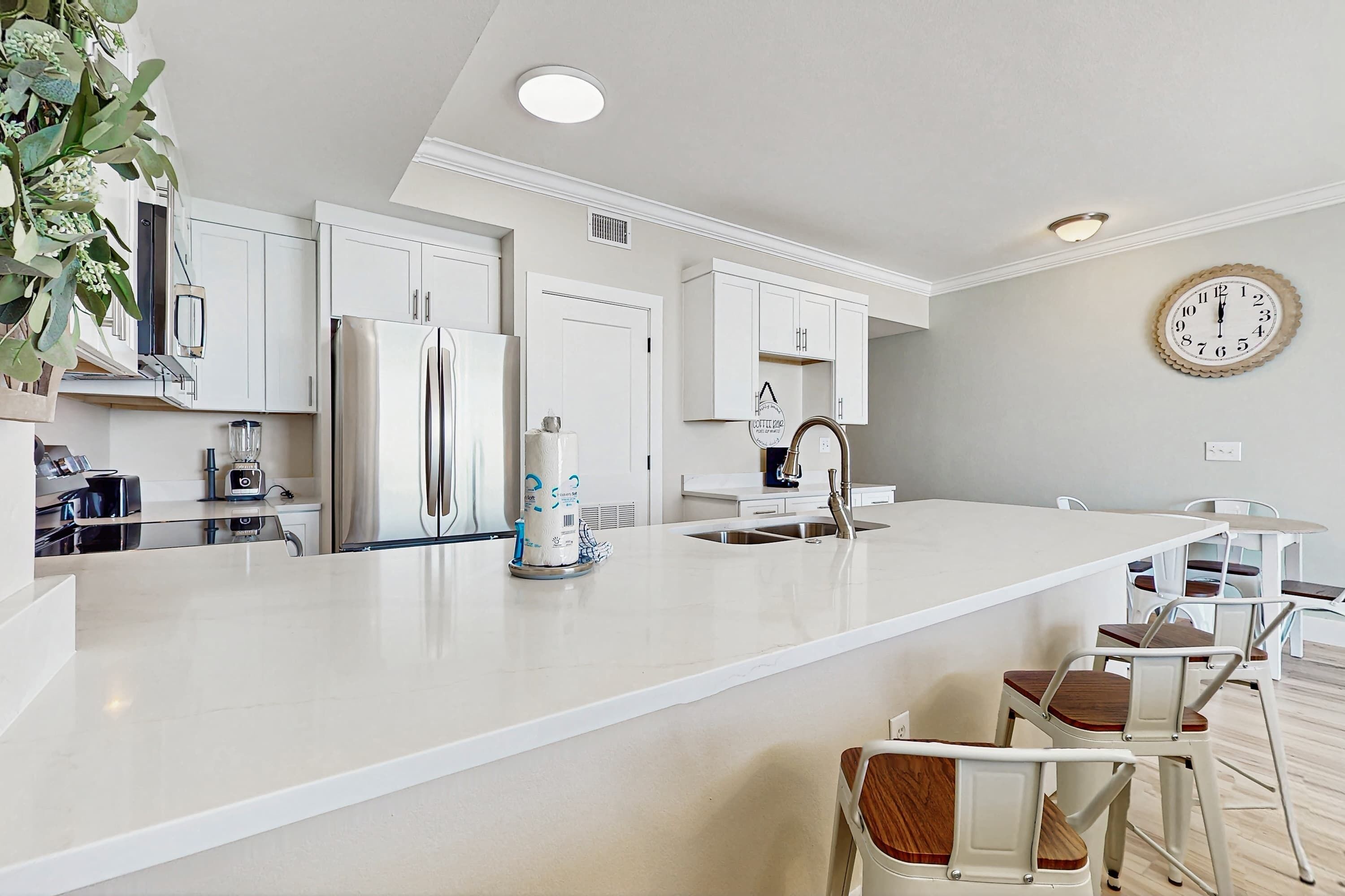 A modern kitchen with white cabinetry, a large island, and bar stools.