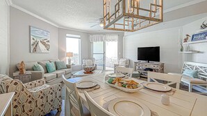 Uma sala de estar espaçosa com uma grande mesa de jantar, assentos confortáveis, televisão e vista para o exterior.