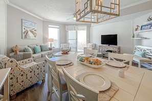 A spacious living room with a large dining table, comfortable seating, a television, and a view to the outside. - Beautifully decorated oceanfront condo with resort pool, & huge walk-in showers (Santa Rosa Beach)