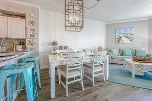 A modern kitchen with white cabinetry, a dining table with chairs, and a hanging light fixture. - Beautifully decorated oceanfront condo with resort pool, & huge walk-in showers (Santa Rosa Beach)