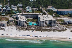 A beachfront hotel with multiple buildings, a swimming pool, and a sandy beach with umbrellas. - Beautifully decorated oceanfront condo with resort pool, & huge walk-in showers (Santa Rosa Beach)