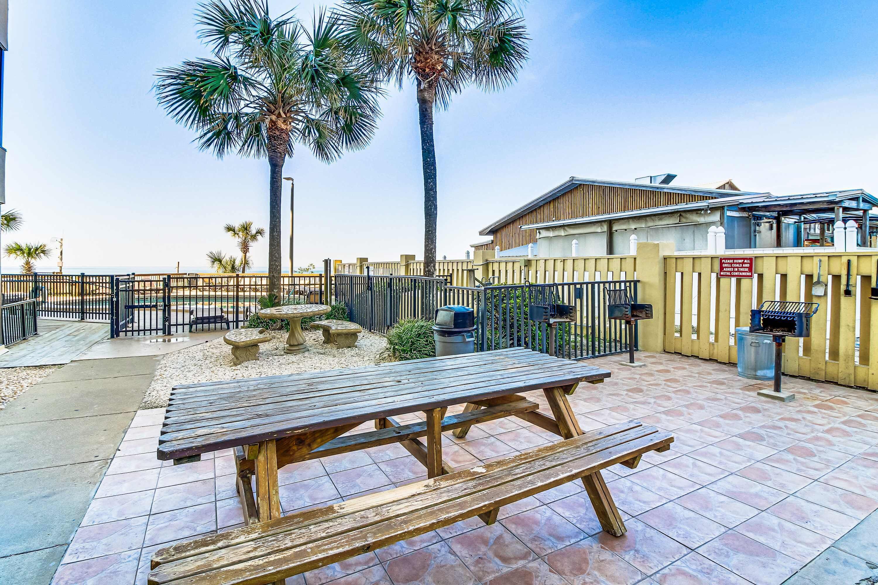 Ein Terrassenbereich im Freien mit Picknicktischen, einem Grill und einem umzäunten Pool.