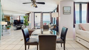 Ein modernes Wohnzimmer mit einem Glastisch, zwei Stühlen, einem Deckenventilator, einem Fernseher und einem Balkon mit Blick.