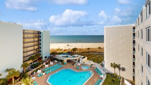 Uma área de piscina de hotel com vista para a praia, várias varandas e cadeiras de espreguiçadeira.