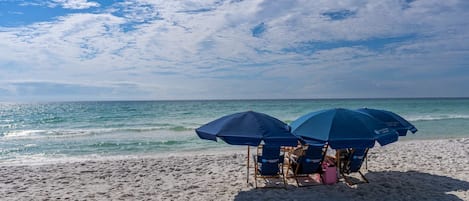 A beach with two blue umbrellas and beach chairs.