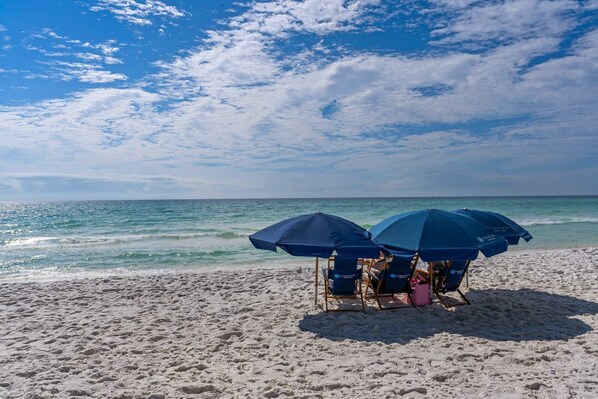 Ein Strand mit zwei blauen Sonnenschirmen und Liegestühlen.