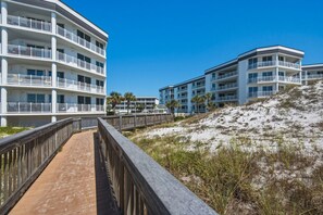 Ein Strandhotel mit mehreren Balkonen, einer Holzpromenade und sandigem Gelände.