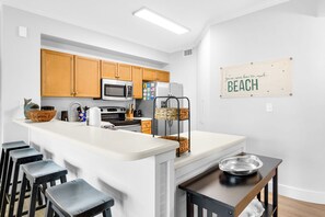 Eine moderne Küche mit einer zentralen Kochinsel, Barhocker, Mikrowelle, Backofen, Kühlschrank und einem an der Wand befestigten Schild.
