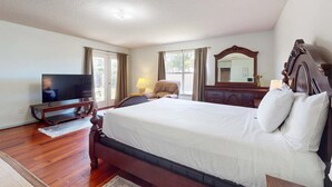 Um quarto com uma cama grande, televisão, cadeira, cômoda e espelho.