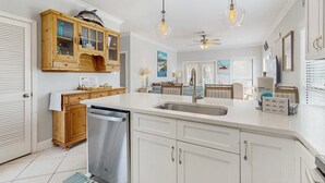 A modern kitchen with white cabinetry, a stainless steel dishwasher, and a wooden cabinet with glass doors. - Gorgeous coastal townhome with private balcony/porch, W/D, and shared pool (Pensacola)