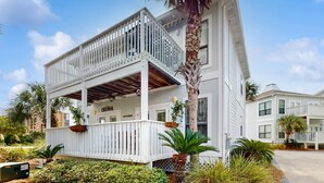 A two-story building with a white exterior, a balcony on the upper floor, and a palm tree in the foreground. - Gorgeous coastal townhome with private balcony/porch, W/D, and shared pool (Pensacola)
