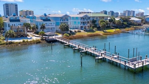 A waterfront property with a dock extending into the water, surrounded by colorful buildings and a clear sky. - Gorgeous coastal townhome with private balcony/porch, W/D, and shared pool (Pensacola)