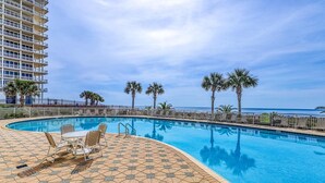 Piscina com deck ladrilhado, espreguiçadeiras e palmeiras.