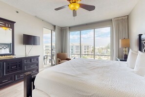 A hotel room with a large bed, a ceiling fan, a TV, and a view of the city through large windows. - Elegant abode overlooking the pool with beach access, tennis & pickleball (Seacrest)