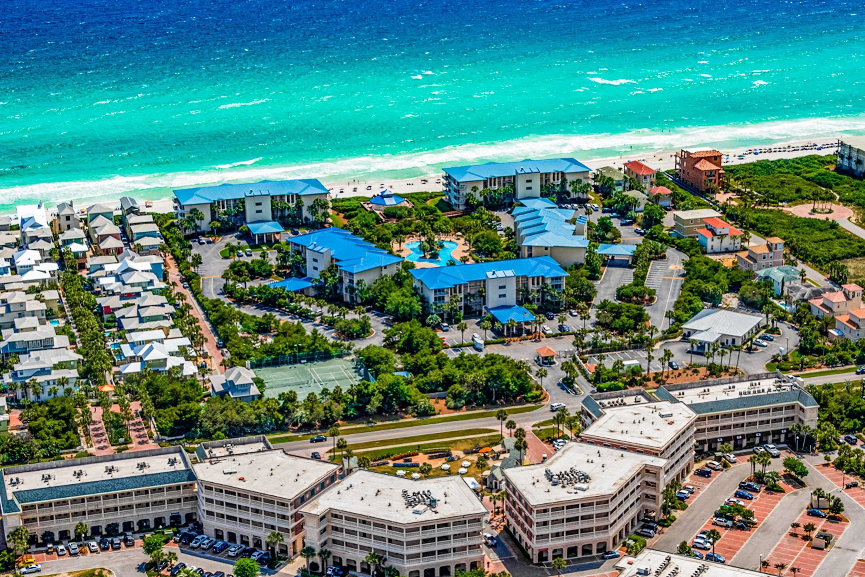 An aerial view of a coastal hotel with multiple buildings, a swimming pool, and a beach in the background.