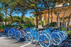 A row of blue bicycles parked in a lot with trees and a building in the background. - Snowbird-friendly condo with pickleball on the beach close to shops & dining (Seacrest)