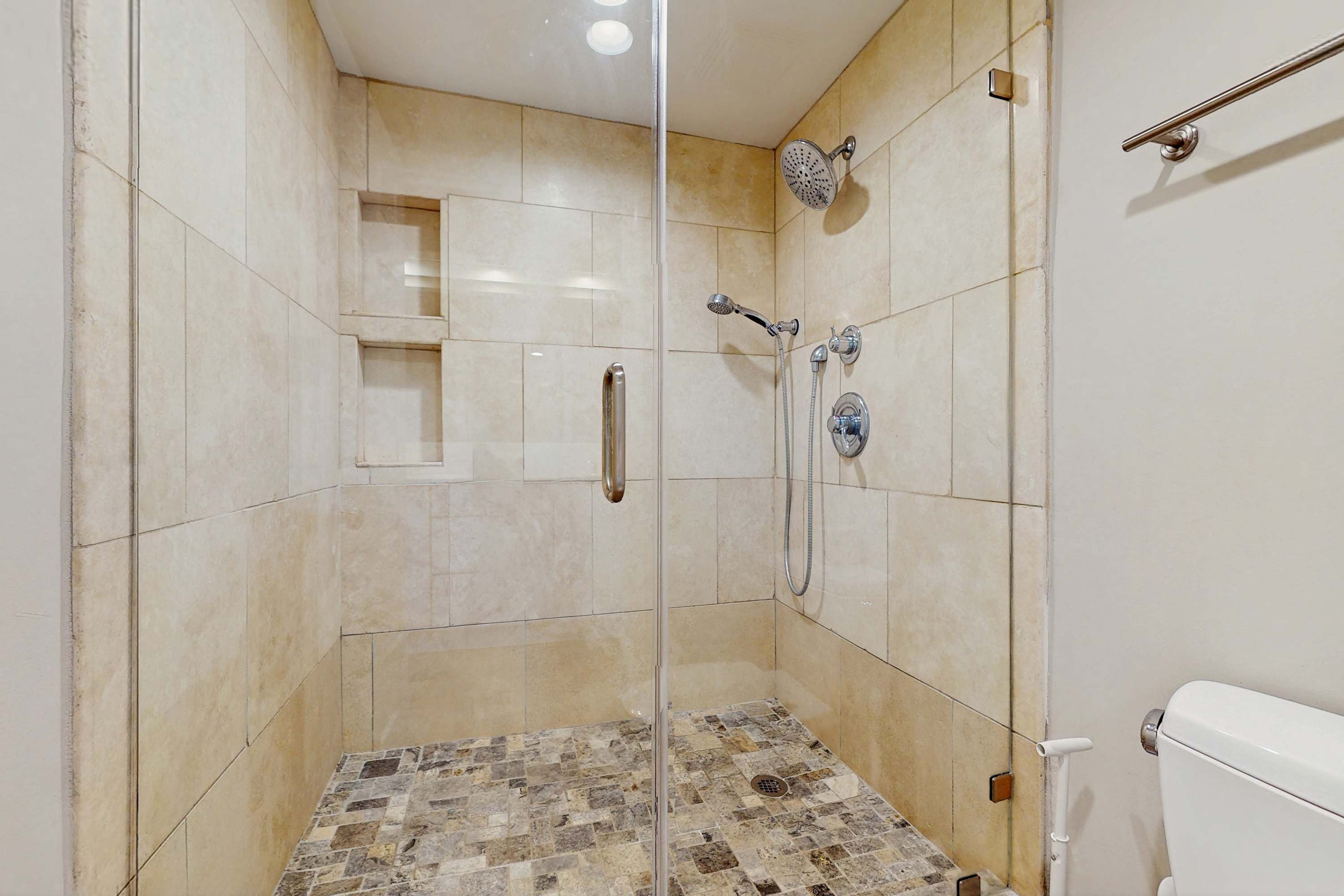 Eine begehbare Dusche mit Glastür, Duschkopf, Handbrause und einer rechts befindlichen Toilette.