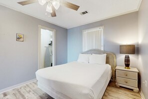 Ein Schlafzimmer mit Bett, Nachttisch, Lampe, Deckenventilator und einer Tür zu einem Badezimmer.