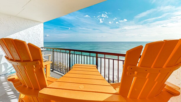 A balcony with two wooden chairs and a table, overlooking a beach and the ocean. - Beachfront condo with Gulf views, pool, tennis courts, & balcony (Fort Walton Beach)