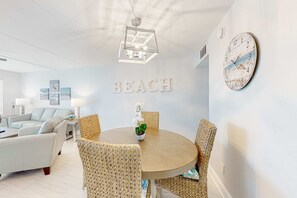 A modern living room with a round wooden table, wicker chairs, and a wall clock. - Beachfront condo with Gulf views, pool, tennis courts, & balcony (Fort Walton Beach)