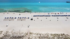 Een strand met rijen ligbedden en parasols, een pier op de achtergrond en een helder uitzicht op de oceaan.