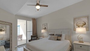 Een slaapkamer met een groot bed, een plafondventilator, een nachtkastje met een lamp en uitzicht op het balkon.