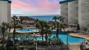 Een resort met een zwembadgedeelte, palmbomen en uitzicht op de oceaan.