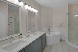Ein modernes Badezimmer mit einem großen Spiegel, zwei Waschbecken, einer Badewanne und einer Duschkabine aus Glas.