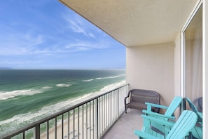 A balcony with a view of the ocean, a wicker chair, and a blue chair. - Elegant condo w/ gulf-front views & on-site pools, hot tubs, beach service (Panama City Beach)