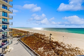A beach view from a hotel balcony with a deck, beach access, and a clear sky. - Incredible beachfront getaway with views, pools, & tennis - Snowbirds welcome (Panama City Beach)