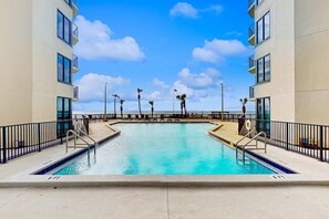 A swimming pool with clear blue water, surrounded by a concrete deck and black railings. - Incredible beachfront getaway with views, pools, & tennis - Snowbirds welcome (Panama City Beach)