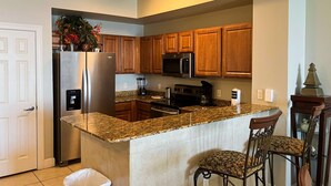 A kitchen with granite countertops, stainless steel appliances, wooden cabinets, and a bar area with two chairs. - Cozy beachfront condo with private balcony, shared pool & beach access (Panama City Beach)