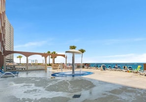 Zona frente a la playa con una fuente de agua, sillas de descanso y un edificio de diseño arquitectónico singular.