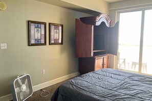 A bedroom with a bed, a standing fan, and two framed pictures on the wall. - Cozy beachfront condo with private balcony, shared pool & beach access (Panama City Beach)