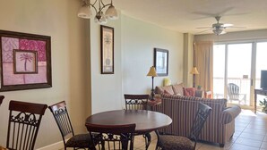 A dining area with a round table and chairs, a sofa, and a ceiling fan. - Cozy beachfront condo with private balcony, shared pool & beach access (Panama City Beach)