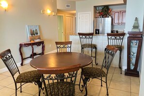 A dining area with a round wooden table and six chairs with patterned upholstery. - Cozy beachfront condo with private balcony, shared pool & beach access (Panama City Beach)