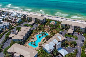 An aerial view of a resort with multiple buildings, a swimming pool, and a beach. - Gorgeous beach condo with furnished balcony, panoramic view & pickleball (Seacrest)