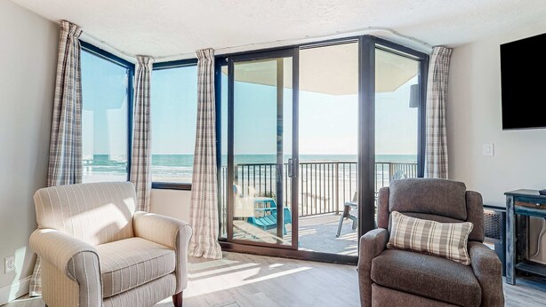 Ein Zimmer mit zwei Sesseln und einer großen Schiebeglasdoor, die auf einen Balkon mit Meerblick führt.