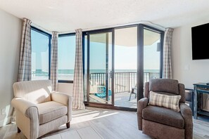 A room with two armchairs, a large sliding glass door leading to a balcony with a view of the beach. - Gulf-front condo with amazing views, WiFi, central AC, pools, & fitness room (Panama City Beach)