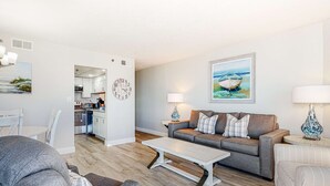 Ein modernes Wohnzimmer mit einem grauen Sofa, einem weißen Couchtisch und einem grauen Sessel. Im Hintergrund ist eine Küche erkennbar.