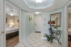 A hotel hallway with a bed, a ceiling fan, a door, a mirror, and a small table with plants. - Spacious condo in with free WiFi, pool access, central AC, and washer&dryer (Fort Walton Beach)